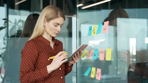 Creative businesswoman using tablet and sticky notes for project planning in professional office.