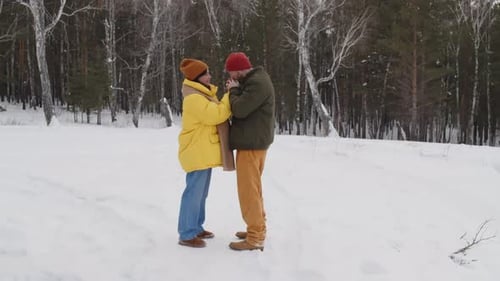 Full Shot of Couple Standing in Snowy Forest, Warming Their Hands