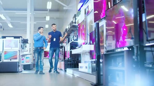 In the Electronics Store Professional Consultant Shows Latest 4K UHD TV's to a Young Man, They Talk