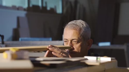 Man Inspecting Wooden Plank in a Dim Workshop