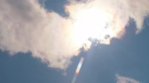 Sunlight Streaming Through Fluffy Clouds in Blue Sky