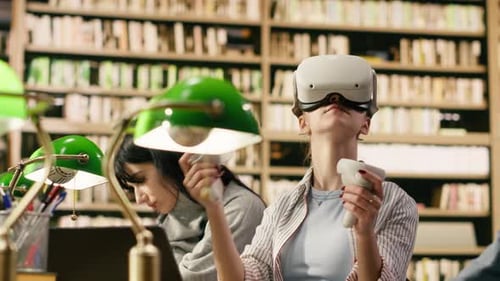 Student Wears VR Glasses and Holds Controllers in University Library