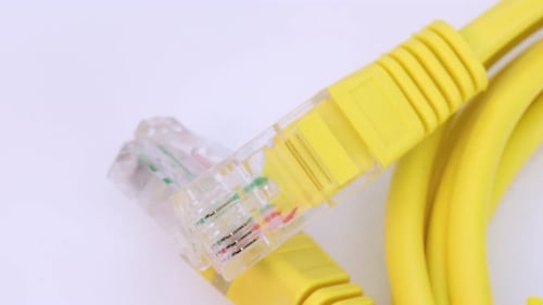 Detail shot of ethernet cable of yellow plastic rotating on white surface, close up view from above