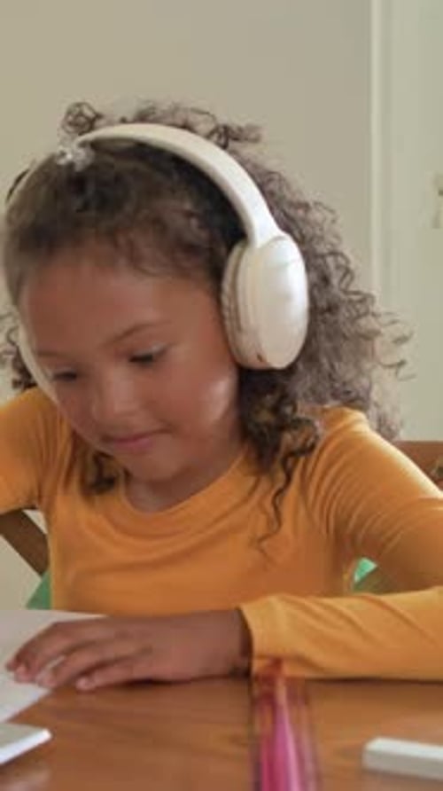 Vertical video: Writing girl in yellow top at table following laptop using red pencil raising hand