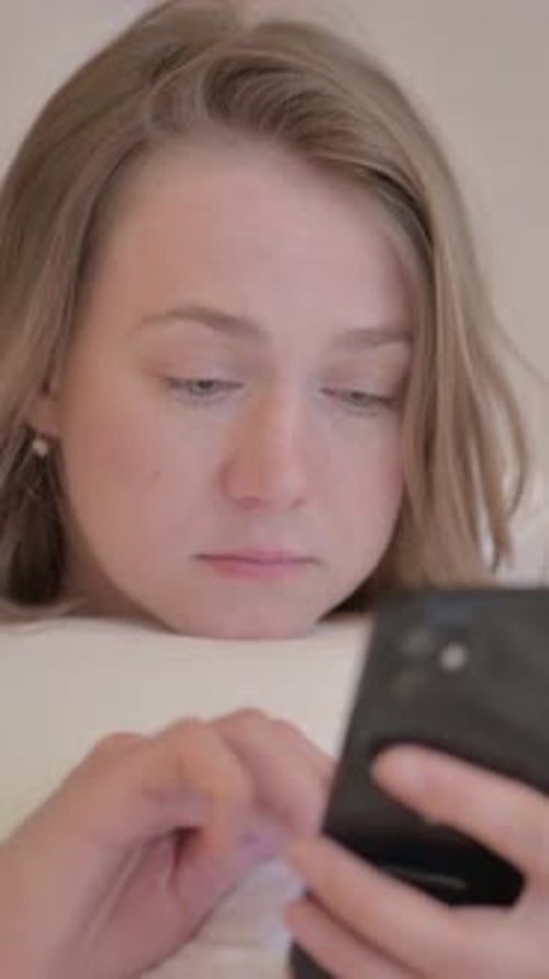 Young Woman using Smartphone while Lying on Stomach in Bed, vertical video