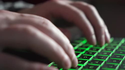 Ein Mann tippt Text auf einer Laptop-Tastatur mit grüner Hintergrundbeleuchtung