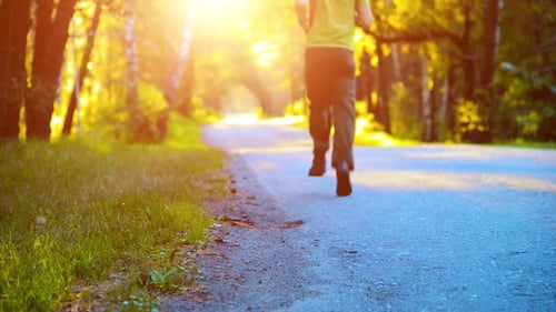 Sport Man Running at Asphalt Road Rural City Park Green Tree Forest and Sun Rays on Horizon