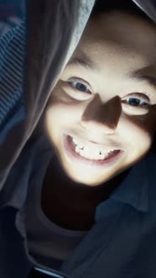 Vertical of Playful Little Girl Making Funny Scary Face Under Blanket at Night