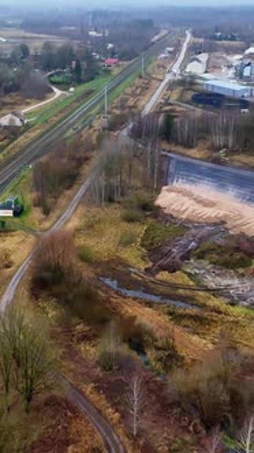 Aerial view of a small white car driving along a narrow muddy countryside road beside railway