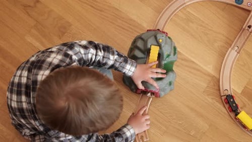 Boy Plays with Toy Train Set on Floor