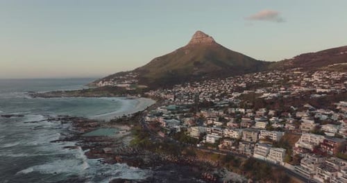 Drone flies high and sideways over Camps Bay beach in Cape Town, South Africa - the sunset-lit Lion'