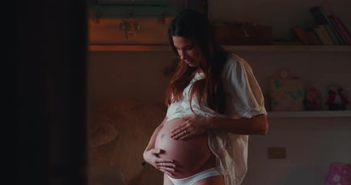 Authentic close up shot of an young pregnant woman in white dress is caressing her belly just woke