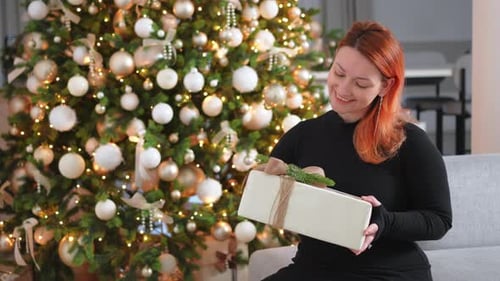 Woman Opening Christmas Gift Near Decorated Tree