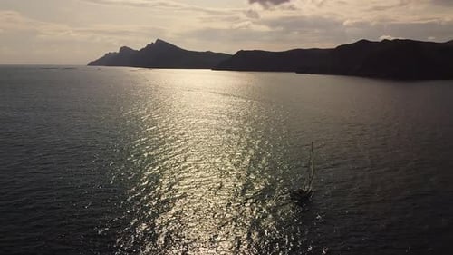 Sailboat sailing by coastline seashore against sunset and mountains. Sail boat in the coast of Spain