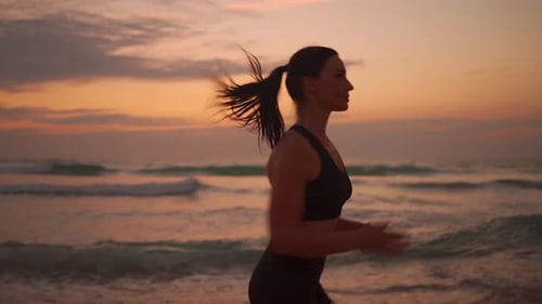 Athletic Woman with Waving Hair Running on Beach at Dramatic Sun Background