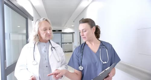 Caucasian female doctors in discussion using tablet in hospital corridor, slow motion