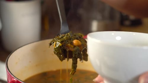 Scooping a ladle of kale and chickpea soup into a serving bowl - close up