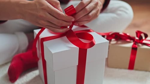 Person Tying a Festive Red Ribbon on Gift Box