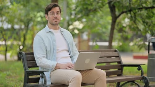 Man Using Laptop on Park Bench Smiles