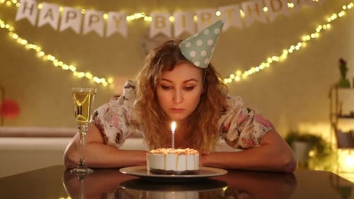 A Woman in a Nice Dress and a Lays Hear Head on the Table and Blows Candles on the Cake