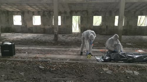 Two forensic specialists gather evidence and put the corpse in a black body bag. shot