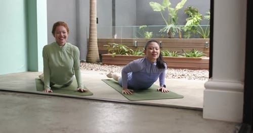 Diversas amigas presionándose las manos, levantándose hacia atrás sobre dos colchonetas en la puerta practicando yoga