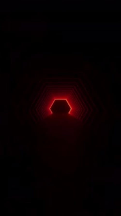 A person walks through a dark tunnel illuminated by neon lights on the concrete floor.