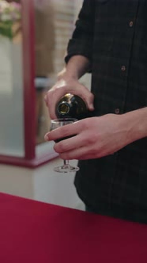 Person gießt Rotwein in ein Glas am Tisch