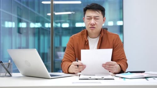 Stressed Man Reviews Documents in Office Workplace