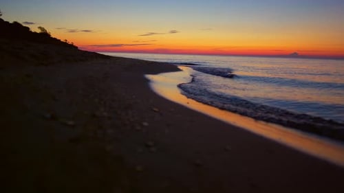 Golden sunrise reflecting on tranquil seashore with mountain silhouette