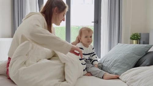 Young mother caressing and soothing her upset toddler son lying in bed