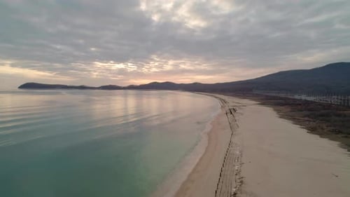 Aerial View of Beach with Calm Transparent Sea Water and Sky Reflection at Sunset Camera Moves
