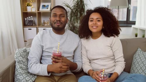Couple on sofa drinking fruit smoothie, talking to camera