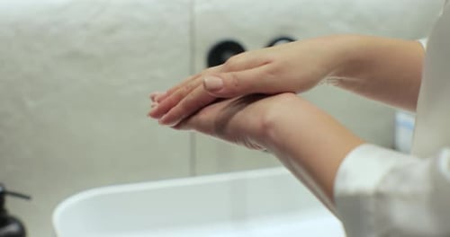 Adult Rubbing Lotion Into Hands in Bathroom