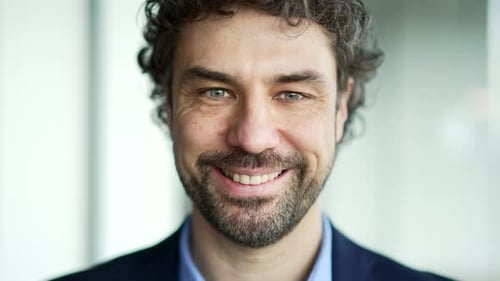 Porträt eines glücklichen bärtigen Unternehmers in einem formellen Anzug, der am Arbeitsplatz im Geschäftsbüro steht.