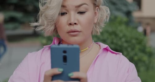 Cute Asian Girl Messaging with Smartphone Touching Screen and Smiling in City Street