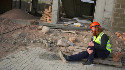 Accident of man worker at construction site is injured and in pain sitting on floor with broken leg.