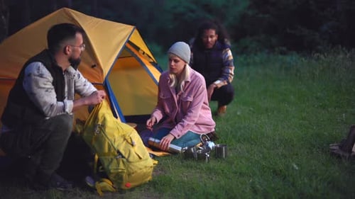 Group of diverse friends setting up their campsite in a peaceful forest clearing during the evening,