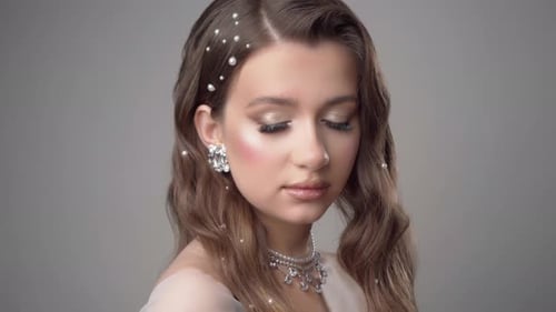 Una hermosa chica con joyas, maquillaje y peinado mira tímidamente a la cámara.