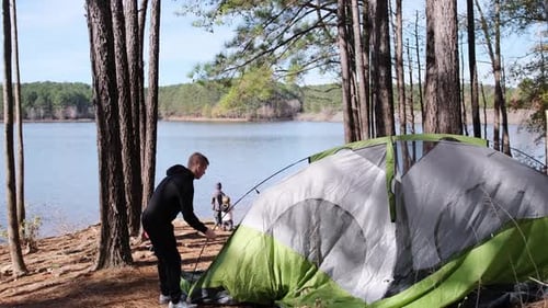 A Man Sets Up a Tent By a Serene Lake Ready for a Night Outdoors