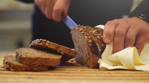 4K Slow motion close up of a a fresh whole-grain bread being sliced with a knife. Grains falling of
