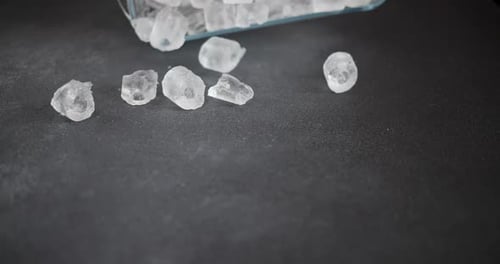 Slow Motion Macro Shot of Ice Cubes Falls on a Dark Background From a Glass Baking Dish