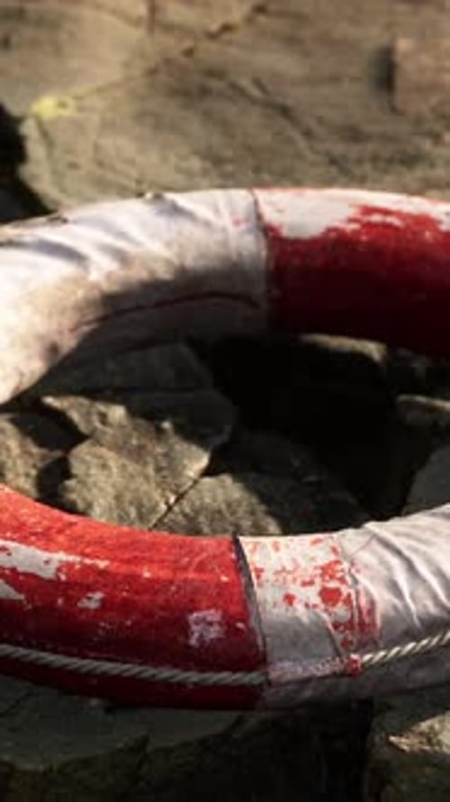 Weathered Red and White Lifebuoy on Rocky Shore Vertical