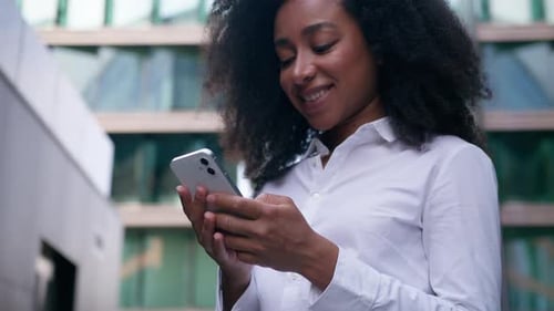 Smiling African American Business Woman Using Mobile Phone Chatting Online in City Businesswoman
