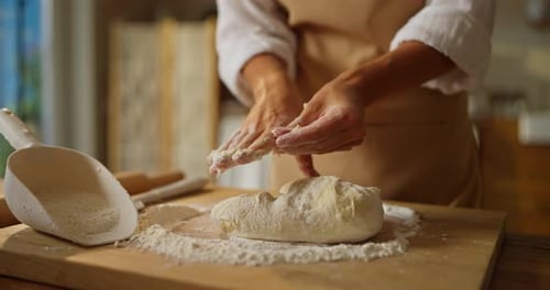 Close Up a Baker Girl in a White Shirt and Beige Apron Kneads the Dough with Her Hands While
