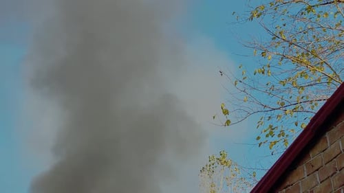 Heavy Smoke Rising into Blue Sky near Building