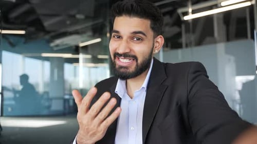 POV Smiling businessman talking on a video call using mobile phone in office. Happy worker in formal
