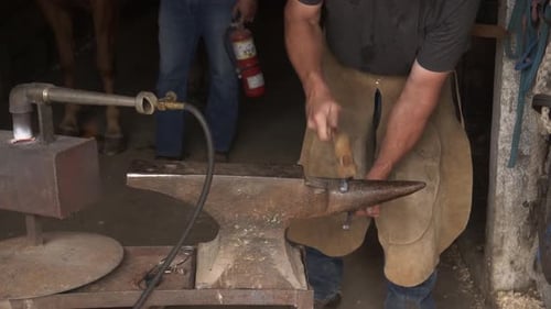 Man Forming Horseshoe at Anvil in Rustic Workshop
