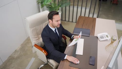 Businessman working with computer, holding business documents reading reports - high angle top down