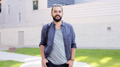 Smiling hipster man with backpack walking along city street in eastern europe